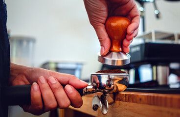 Close-up of hand Barista cafe making coffee with manual presses ground coffee using tamper at the coffee shop