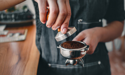 Close-up of hand barista or coffee maker holding portafilter and coffee tamper making an espresso...