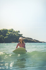 Young woman surfer in pink special swimming suit and hat going to surfing. Outdoors. Hiriketiya Beach, Dikwella. Sri Lanka. Tropical coastline. Vertical format.