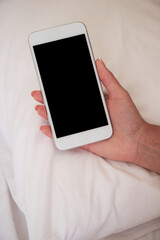 Young woman uses smartphone while lying on bed. Empty smartphone screen. Mocap for mobile app