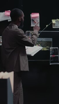 Vertical video: Young policeman examining detective map with evidence, trying to solve crime or felony. Male inspector doing detective work and background checks, using case files for research
