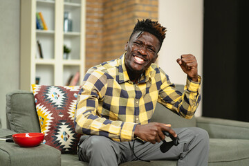 Young happy African guy playing video game at home. Man holding joystick and playing video games