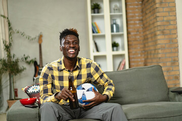 Young African man watching sport match on television and supporting his favorite team. Happy man enjoying victory, watching sports competition on tv.