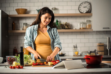 Beautiful pregnant woman preparing delicious food. Smiling woman cooking pasta at home