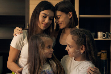 Staged photo. Lesbian couple and their children in the kitchen. The kids are the main chefs. We can paint with flour! Everyone is covered in flour, but no one is angry. They are all smiling.