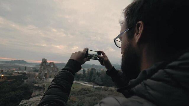 Man travel blogger vlogger taking photo on smartphone evening antique ruins building