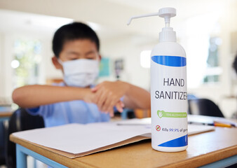 Boy rubbing hand sanitizer for hygiene, safety and protection against covid at school. Closeup bottle of alcohol gel on desk in classroom to clean, kill or prevent the spread of germs or coronavirus
