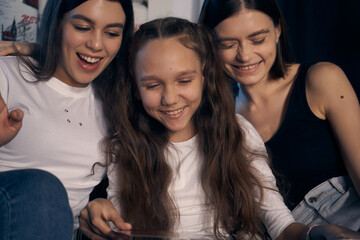 Fototapeta premium Staged photo. Lesbian couple and their kids are having a good time at home. Cozy atmosphere. One of the girls is looking at a picture book with her parents. They are all laughing.