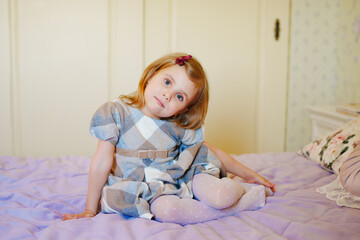 Fototapeta premium a portrait of a cute little girl in a plaid dress in the bed. 