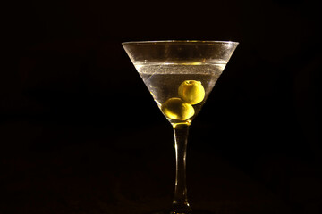 A clear glass of martini, focus on olives on a night club marble bar counter 