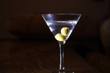 A clear glass of martini, focus on olives on a night club marble bar counter 
