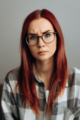 the wary, angry look of the red-haired girl with the glasses and the plaid shirt against the gray background