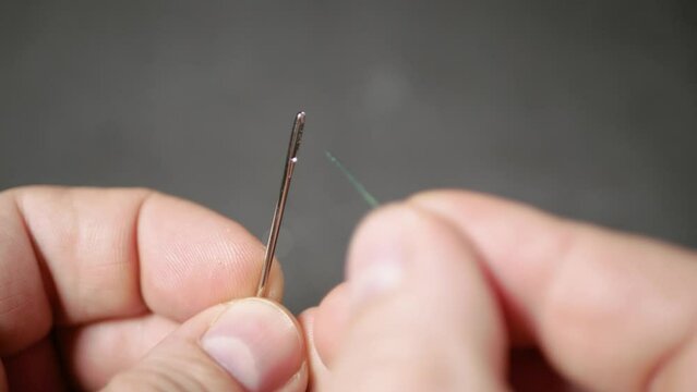 A man inserts a thread into a sewing needle, a man is preparing to sew. Close-up, selective focus.