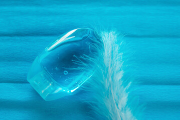 Pocket antiseptic gel in a blue container on a blue background. Air bubbles in the gel. White feather next to antiseptic