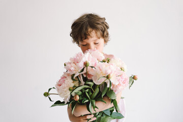 Cheerful happy child with Peonys bouquet. Smiling little boy on white background. Mother's Day. Love and romantic concept