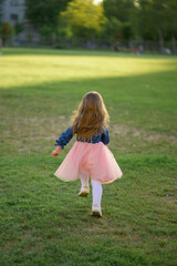 A little girl 3 years old in a summer dress runs away from the camera. The girl is turned back. Summer time.