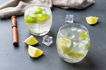 Brazilian lemon caipirinha in glasses with ice and fruit slices over stone background
