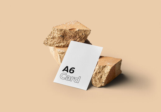 Mockup of customizable vertical color A6 card resting against rocks available against customizable color background