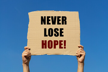 Never lose hope text on box paper held by 2 hands with isolated blue sky background. This message board can be used as business concept about not losing hope.