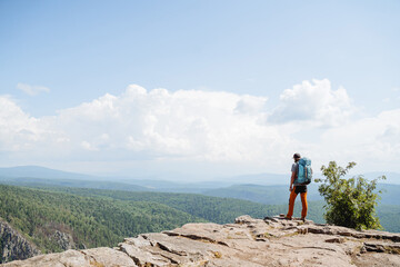 Obraz premium A tourist with a backpack stands on the edge of a cliff high in the mountains against the sky, a beautiful landscape, a mountain peak, trekking on a hike, a climber looks down.
