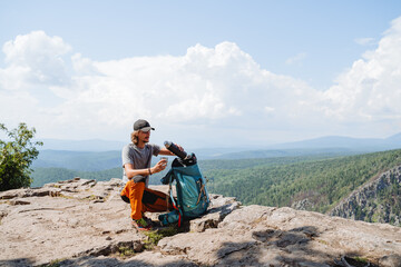 Delicious aromatic tea from a thermos pour into a glass, a guy tourist drinks tea in the mountains on a hike, a large backpack with things, a snack on the way trekking in the mountains