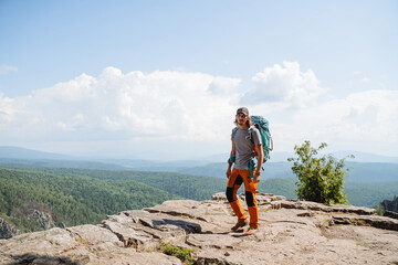 A guy tourist with a backpack walks in a hike in the mountains, a heavy bag on his shoulders, mountain hiking, a man walks alone trekking, a hipster in nature