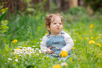 Happy little baby girl sitting on a green meadow with yellow flowers dandelions on the nature in the park