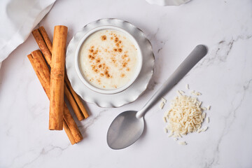 Creamy rice pudding or arroz con leche topped with cinnamon on a white marble background