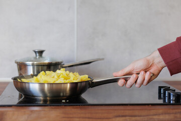 fry potatoes in frying pan at home, woman cooks food on gas stove, stirs vegetables in saucepan. bake and cook raw potatoes. fast food, fat harmful with oil. cooking for dinner or lunch