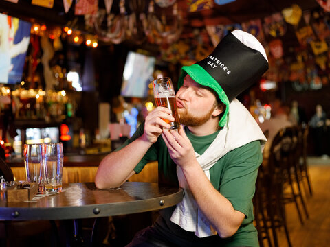 cheerful ginger man in leprechaun hat for st patricks day kissing beer