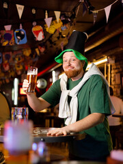 a real ginger guy in a leprechaun hat for st. patrick's day holds a glass of beer