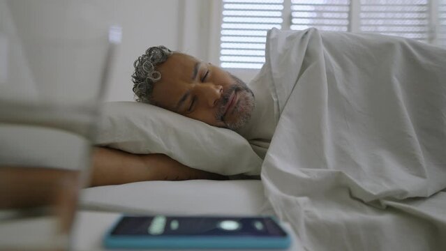 Mobile alarm clock in the morning. Black man sleeping in bed and wake up with message in cell phone. 
