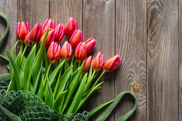 Bouquet of fresh pink tulips in a string bag on a wooden background, top view, concept of mother's day, women's day, spring background with a bouquet of flowers, rustic style.
