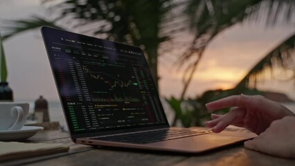 Female cryptocurrency trader at laptop checking candlestick charts online working remotely at outdoor tropical seaside cafe. Woman crypto broker analyses stock exchange rates and bets by ocean closeup - Powered by Adobe