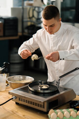 A professional chef in the kitchen of a restaurant prepares pancakes for breakfast. Culinary recipe Frying pan on the stove