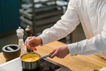 The chef prepares cheese sauce on the stove The work of a professional in the restaurant kitchen