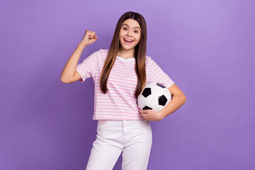 Portrait of delighted funky girl hold football raise fist success achievement isolated on purple color background