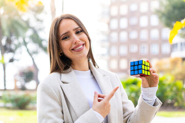 Young pretty woman holding a three dimensional puzzle cube at outdoors and pointing it