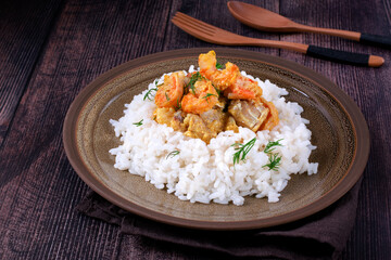 Fish curry with codfish, pollack and shrimps with coconut milk served on rice on brown plate