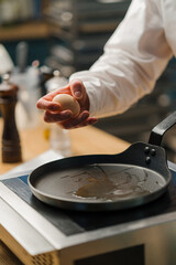 A cook breaks an egg into a pan Preparing breakfast in a professional kitchen