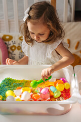 A little girl playing with colored rice and Easter eggs in sensory bin. Easter sensory bin with bright rice and eggs, bunny, carrot. Sensory play and holidays activity for kids. Happy Easter concept.