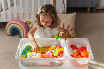 A little girl playing with colored rice and Easter eggs in sensory bin. Easter sensory bin with...