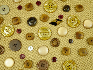 Brown buttons in different designs and sizes for sewing on clothes lie on a white burlap