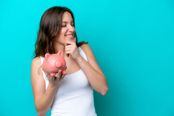 Young Caucasian woman holding a piggybank isolated on blue bakcground thinking an idea and looking side