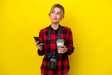 Uruguayan photographer woman isolated on yellow background holding coffee to take away and a mobile while thinking something