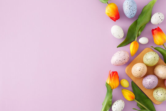 Easter decoration idea. Top view photo of colorful easter eggs in wooden holder and tulips flowers on isolated violet background with copyspace