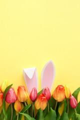 Easter concept. Top view vertical photo of rabbit bunny ears in tulips flowers and colorful easter eggs on isolated yellow background with empty space