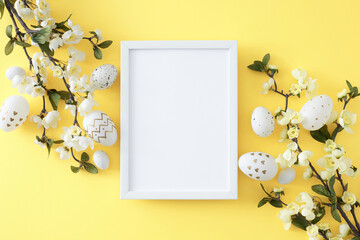 Naklejka na ściany i meble Easter decor concept. Top view composition made of photo frame white golden eggs and spring blossom branch on isolated yellow background with blank space