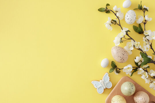 Easter celebration idea. Top view photo of colorful easter eggs in wooden holder and spring blossom branch on isolated yellow background with empty space
