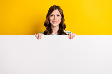 Photo of lovely satisfied woman with curly hairstyle wear striped shirt hold billboard presenting sale isolated on yellow color background